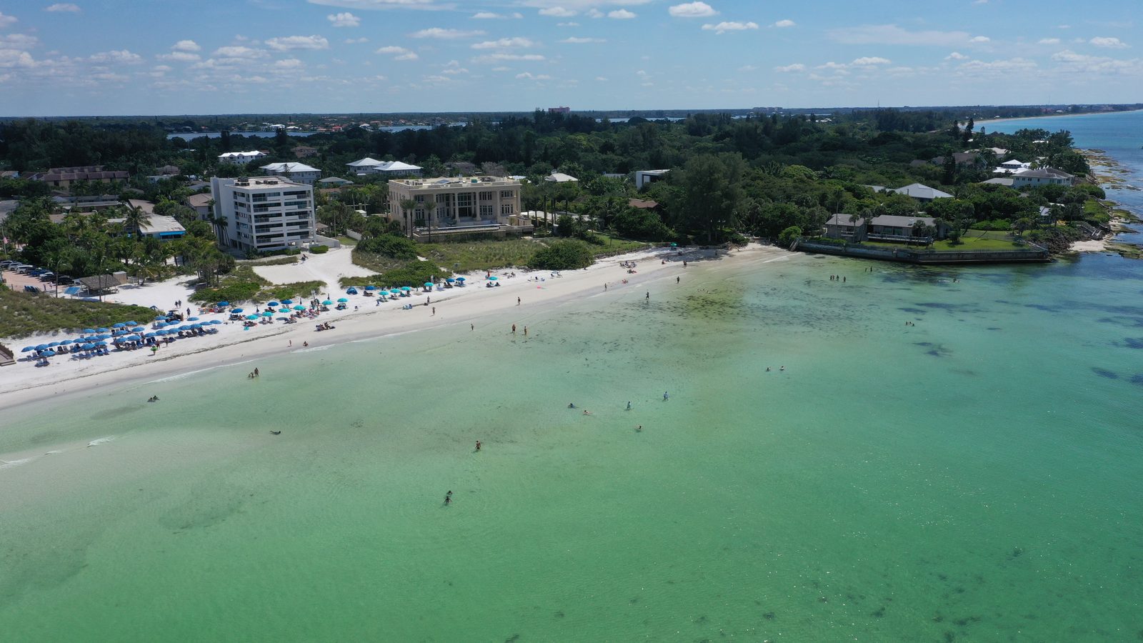 Swimmers in the clear shallows off Crescent Beach on Siesta Key, looking south toward the Point of Rocks outcrop