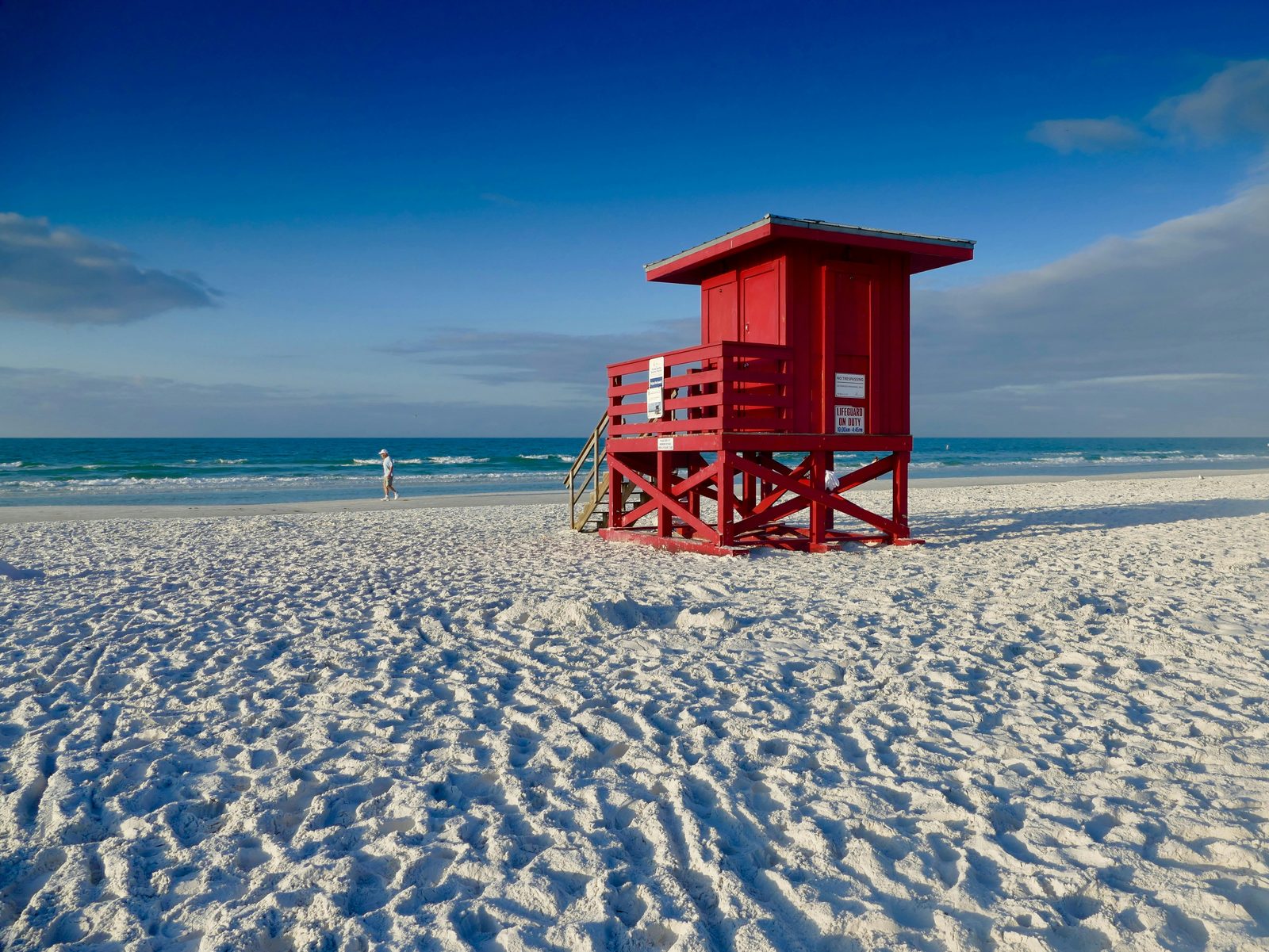 Red lifeguard stand on the white quartz sand of Siesta Beach, with the Gulf of Mexico under a deep blue sky