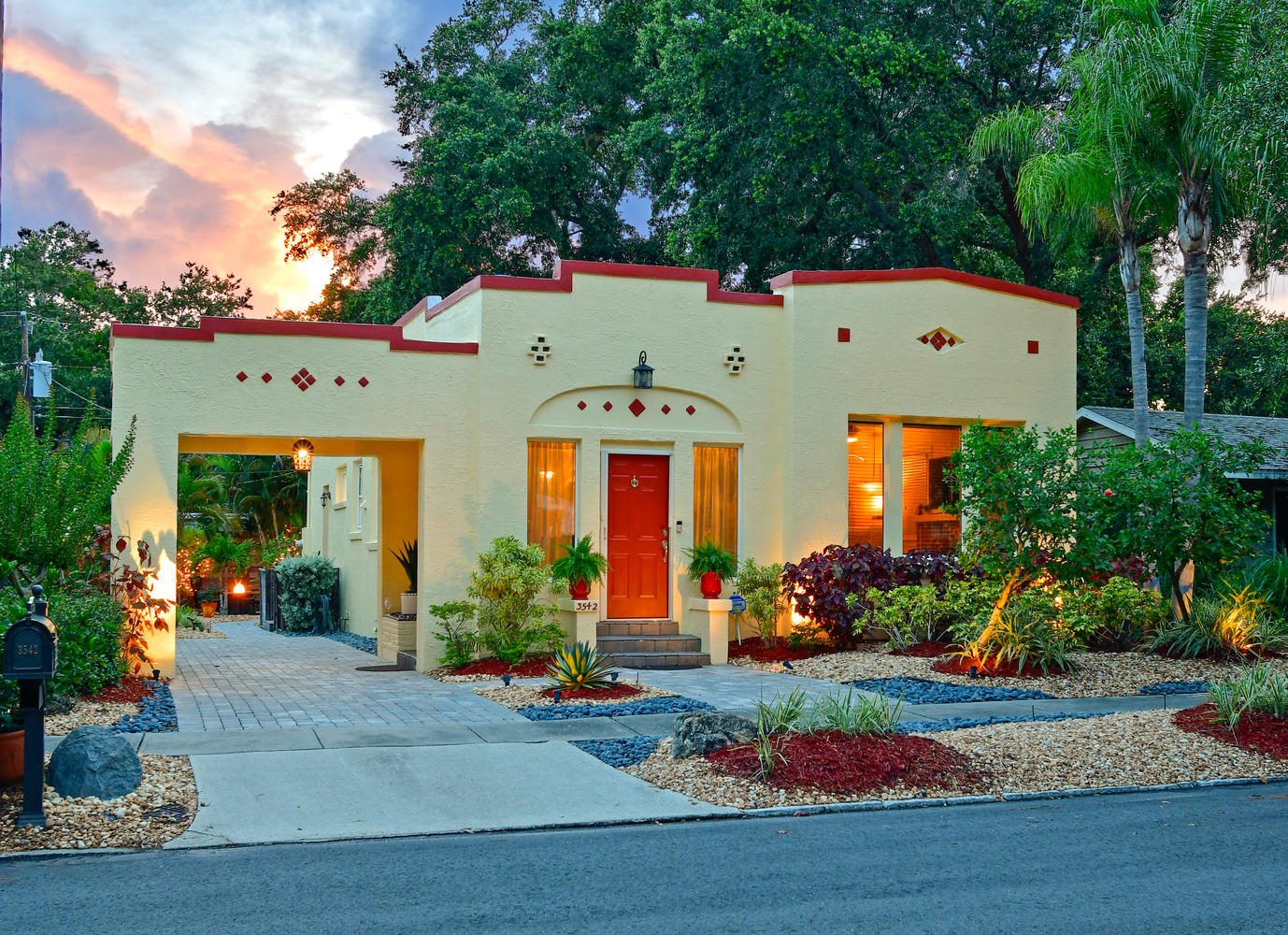 Restored 1920s bungalow on Jacinto Court in Sarasota's Granada neighborhood, glowing at dusk behind tropical landscaping
